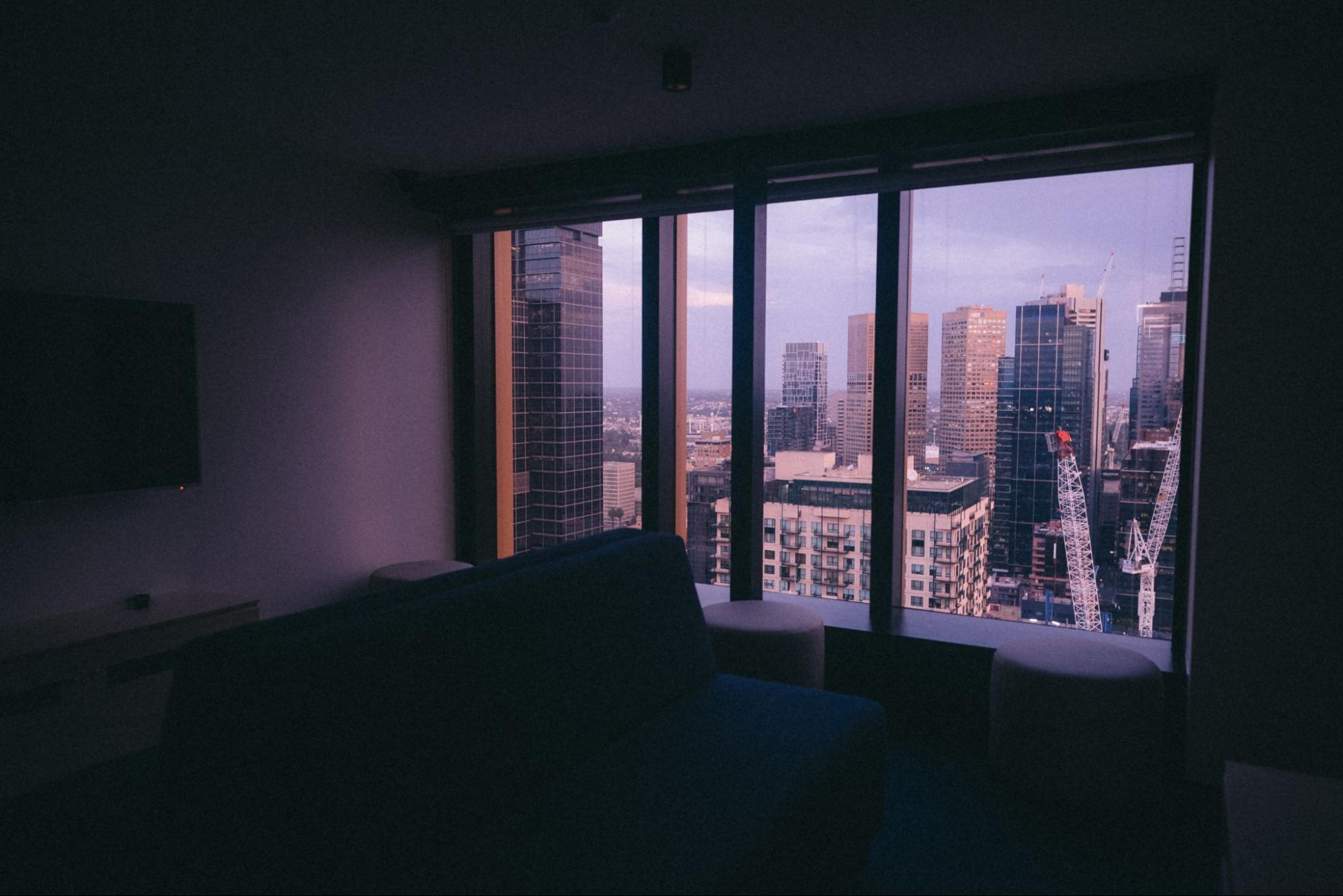A panoramic view of the city skyline seen through a hotel room window, showcasing tall buildings and urban life